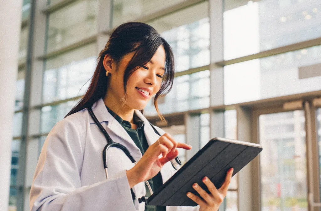 Asian woman, doctor and happy in hospital with tablet for public service, results and committed. Female person, closeup and smile for healthcare with appointment, work and wellness in medical career