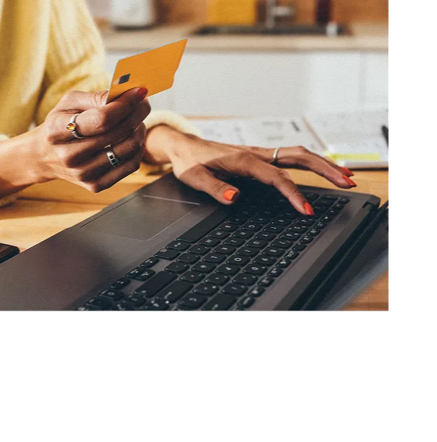 Woman looking at credit card typing in card information to computer for purchase