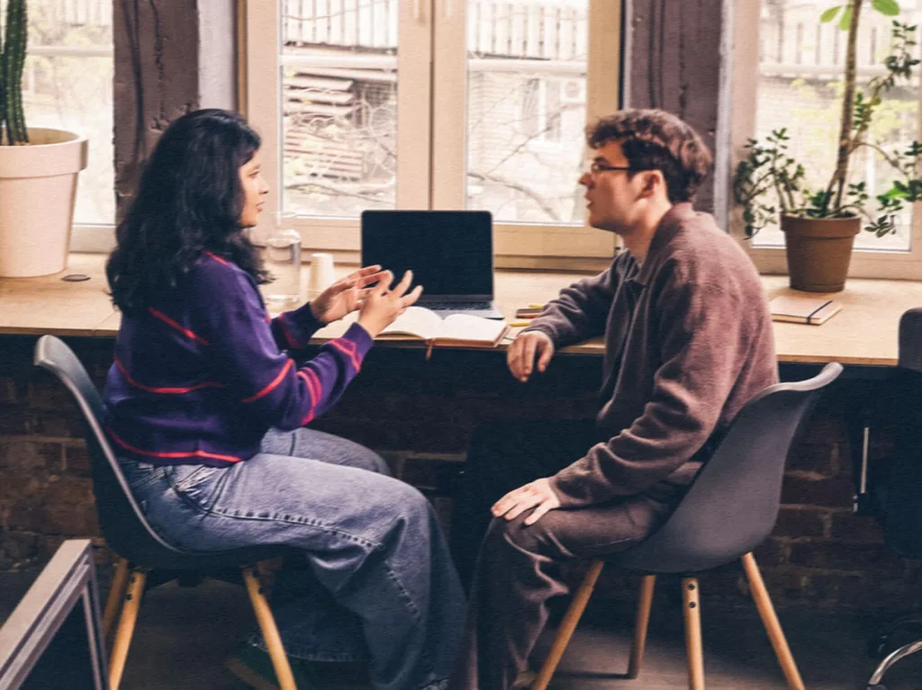 Two people sitting side-by-side at a desk having a discussion