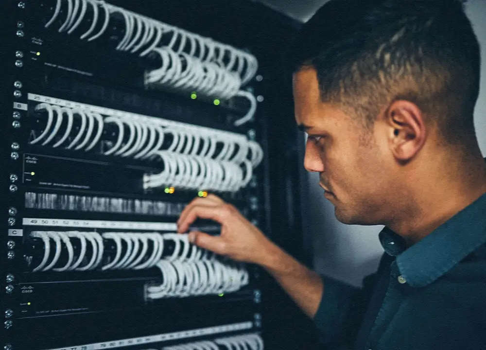 A man in a collared shirt manages network cables for cloud-based servers using disaster recovery services.